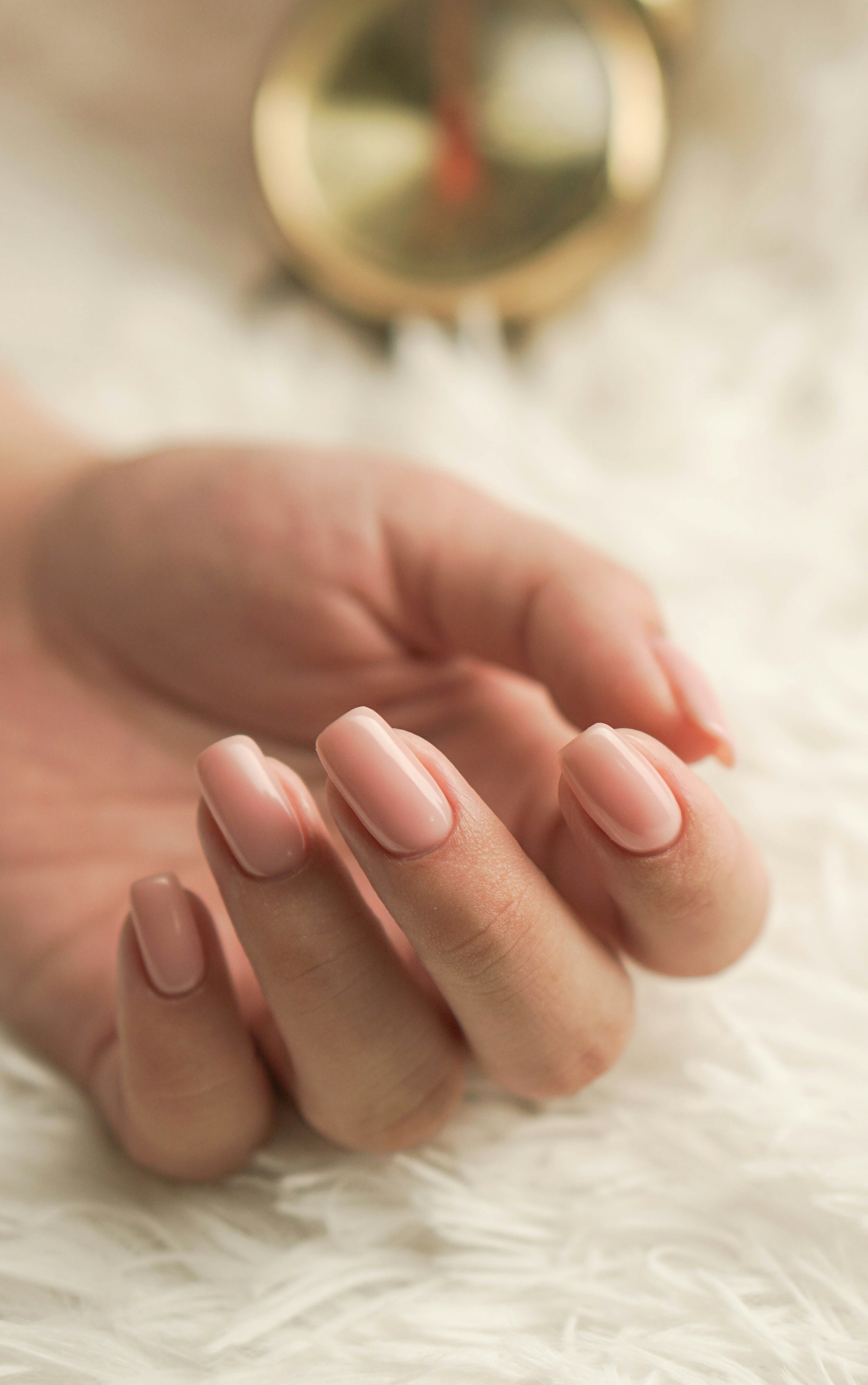 Nude pink gel nails resting on a soft white throw